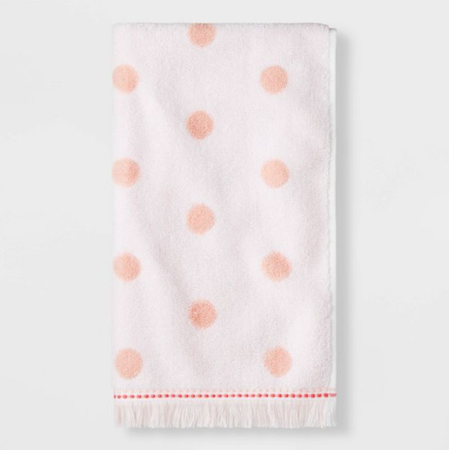 Pink hand towel with polka dots and fringes at the bottom, set against a white background