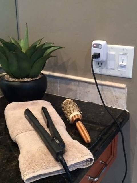 A hair straightener resting on a bathroom counter, plugged into the timer.