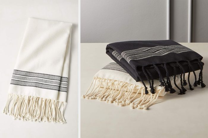 White and gray striped towel folded neatly with white fringes along the bottom, with black and white versions stacked on top of each other on a table