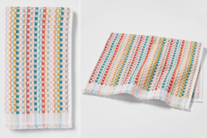 A white towel with rainbow stripes, neatly folded against a white backdrop