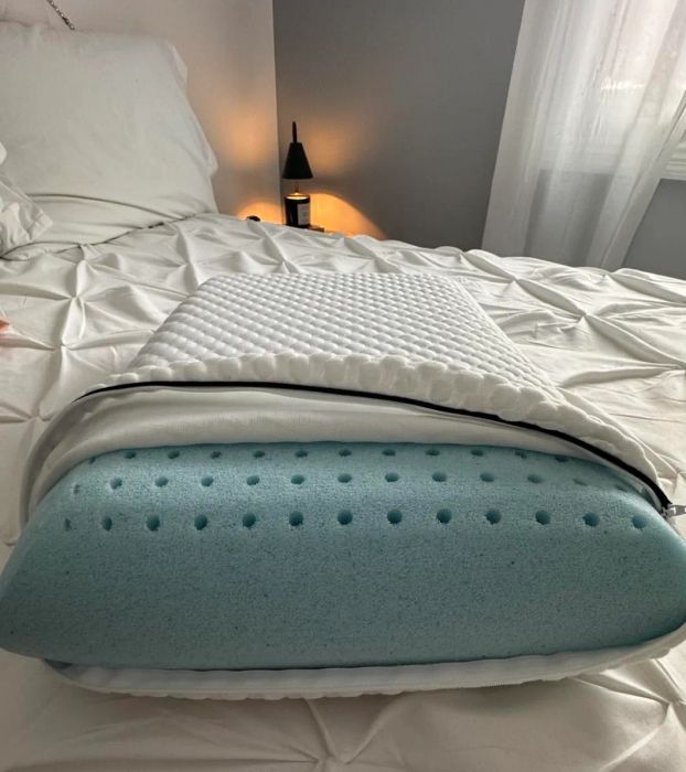 A cozy memory foam pillow with a white quilted cover placed neatly on a bed. A nightstand and lamp are visible in the background.