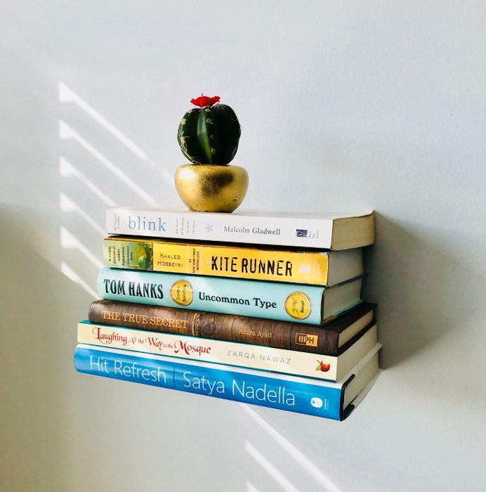 A stack of books resting on the invisible shelf on the wall