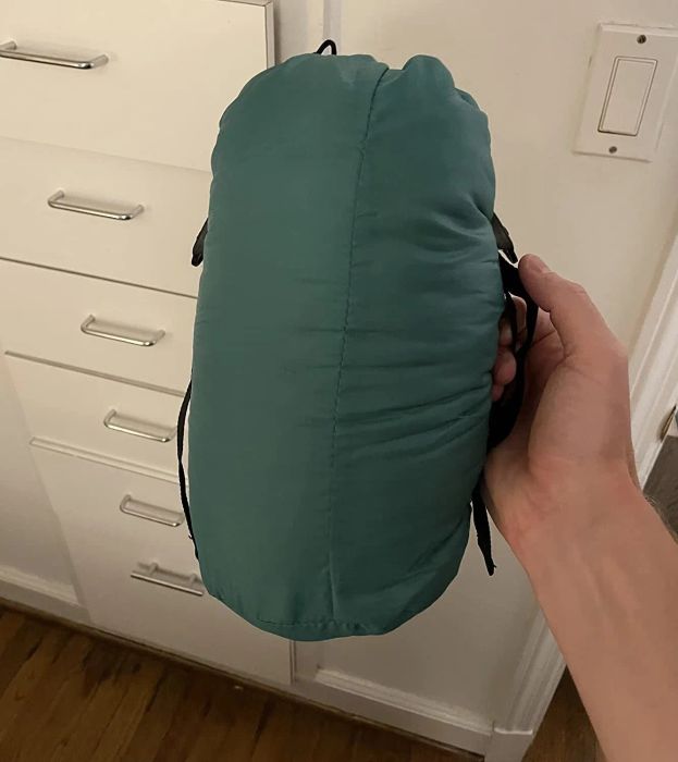 A person holding a compactly rolled sleeping bag inside a home, showcasing its portable design and easy storage.