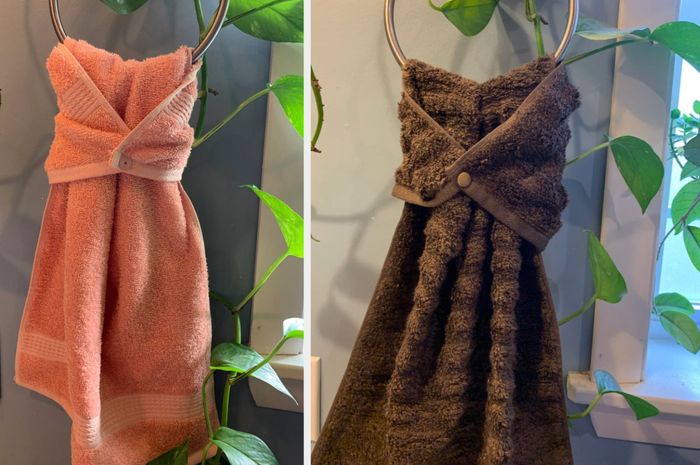 A pink hand towel with a button closure snapped in front, hanging neatly on a towel rack, with a black version displayed beside it