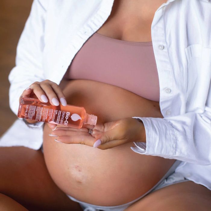 Pregnant model applying a large bottle of Bio-Oil to her belly.