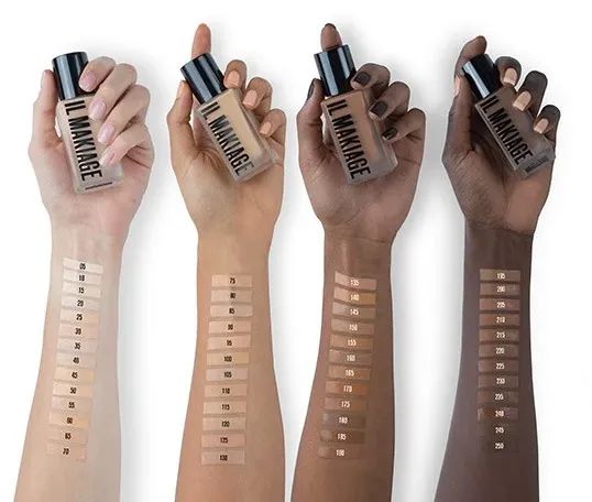 Four models hold bottles of foundation, each showcasing swatches of different shades on their forearms.