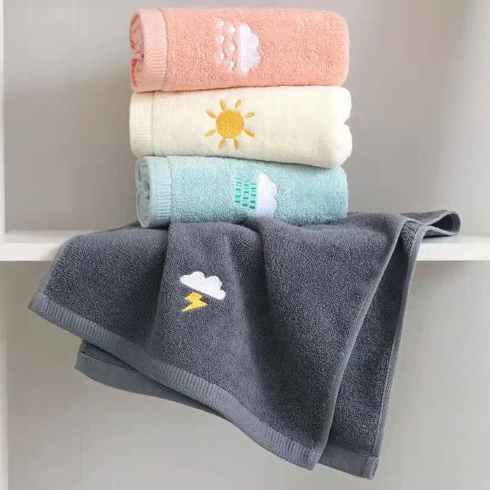 Black, blue, yellow, and pink towels neatly stacked, each adorned with embroidery of clouds, rain, and sunshine