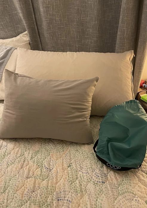 Two pillows placed on a bed alongside a green Coop Home Goods bag, perfect for those shopping for bedding essentials.