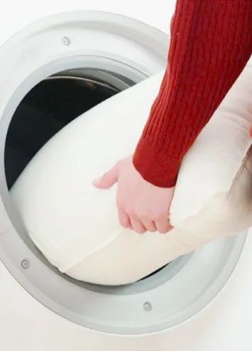A person places the pillow inside a washing machine.