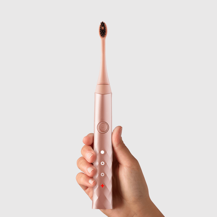 A hand holding a rose gold Burst Oral Care toothbrush