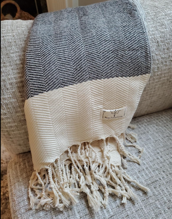A textured woven blanket with tassels casually draped over a couch, a small tag peeking out from the edge of the blanket.