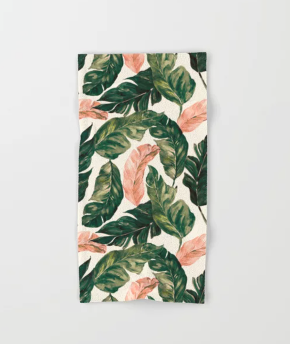 A hand towel with a pattern of pink and green leaves, laid out on a white background