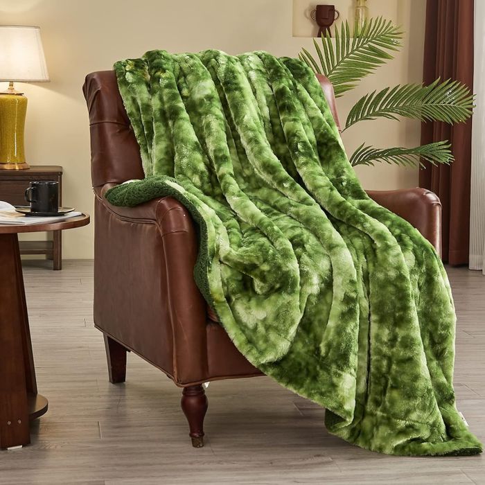 A soft, plush green throw blanket casually draped over a brown leather armchair in a warm and inviting living room.