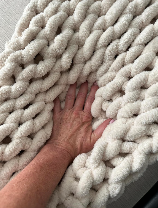 A hand pressing into a soft, chunky knit blanket, showcasing its plush and inviting texture.