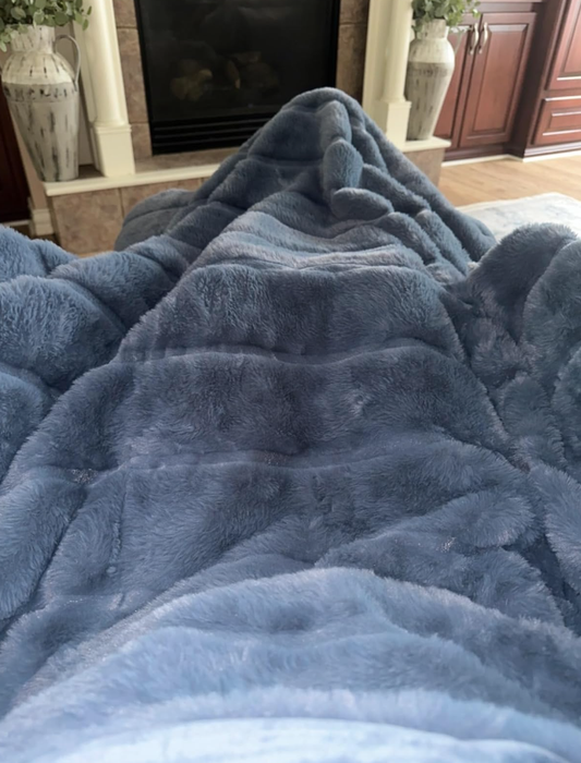 A person relaxing on a sofa, snuggled under a soft and cozy blanket, with a warm fireplace and cabinets in the background.