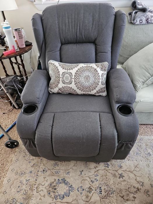 A plush gray recliner with cup holders and a decorative pillow, placed in a warm and inviting living room space.