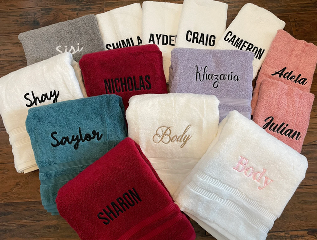 Hand towels in various colors with embroidered names, laid out on a wooden surface
