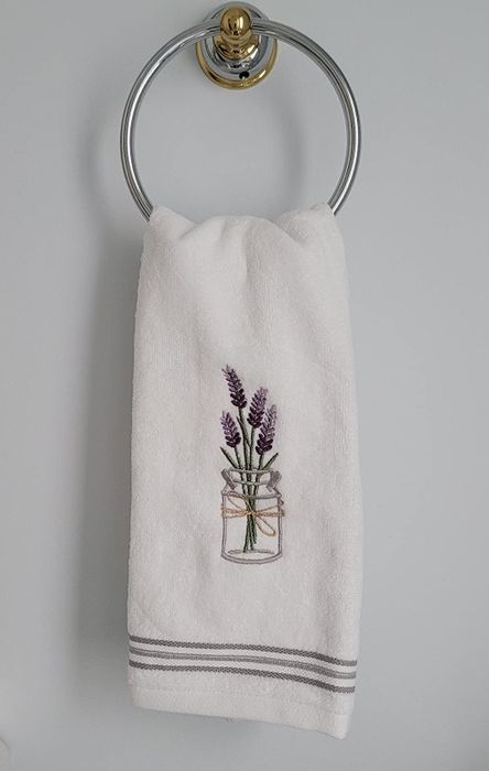 Reviewer image of a lavender embroidered hand towel in white and purple, hanging on a towel hook