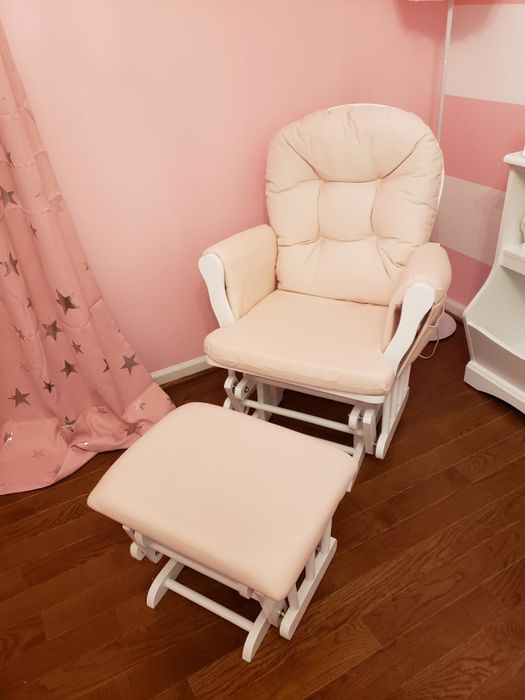 A padded rocking chair with a matching footrest in a pink nursery, complete with star-patterned curtains, wooden flooring, and a white shelving unit.