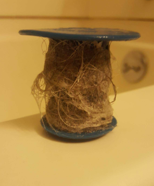 A reviewer's photo showing a clump of hair caught by the TubShroom before it can go down the drain