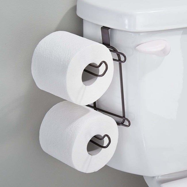 A toilet with a holder on the tank holding two extra toilet paper rolls