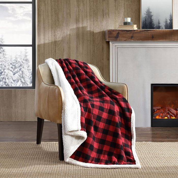 A cozy armchair draped with a red and black plaid blanket sits near a fireplace, with a picturesque snowy landscape visible through the window.