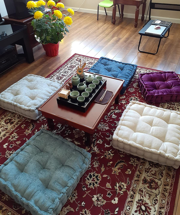 A photo from the reviewer displaying five different colored pillows arranged on the floor surrounding a coffee table
