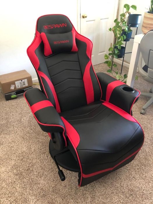 A Respawn gaming chair with padded armrests, a cup holder, and a supportive backrest, placed in a room with a box and a potted plant in the background.
