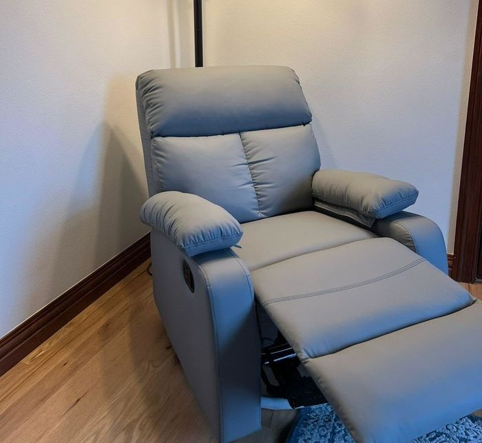 A cozy recliner chair placed under a standing lamp with two light bulbs.