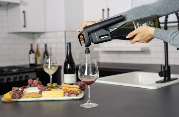 The system is attached to a wine bottle, demonstrating how it pours a glass of wine.
