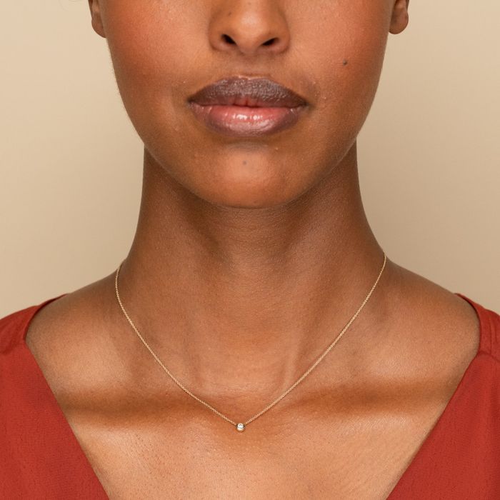 A small round diamond pendant on a gold chain, resting around a model's neck.