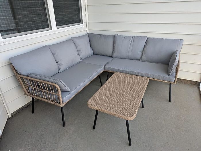 An outdoor patio set including a corner sofa and a matching rectangular coffee table, situated on a porch with white siding