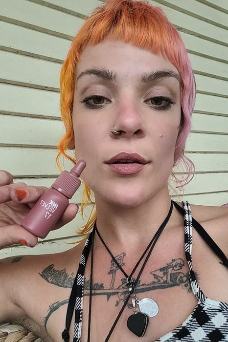 A reviewer sporting a soft pink shade while holding the bottle