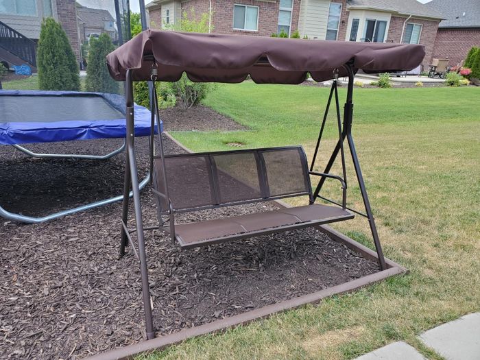An outdoor patio swing with a canopy, set in a backyard. This image is featured in a Shopping article