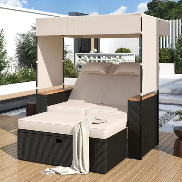 A rattan outdoor daybed featuring a canopy and beige cushions, accessorized with pillows and a cozy throw blanket, placed on a wooden deck in a contemporary outdoor setting