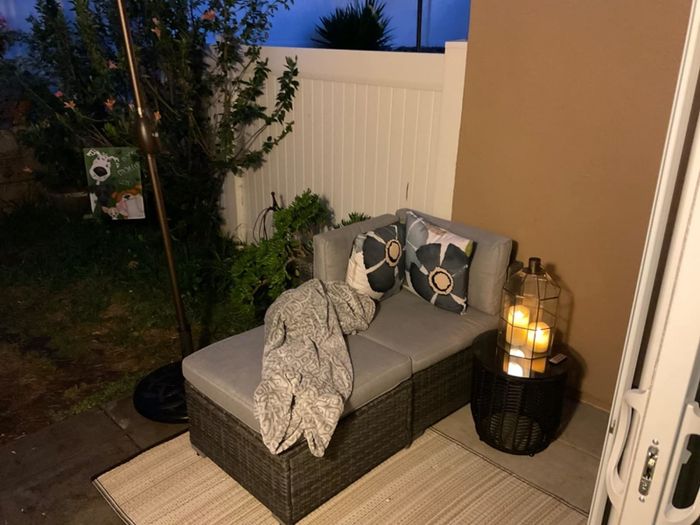 An outdoor patio featuring a lounge chair, blanket, and pillows, with a table holding a lantern and candles nearby, creating a warm and inviting ambiance
