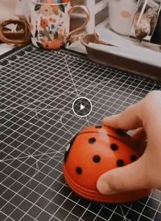 A hand using a ladybug-shaped lint remover on a checkered fabric surface, with decorative mugs in the background