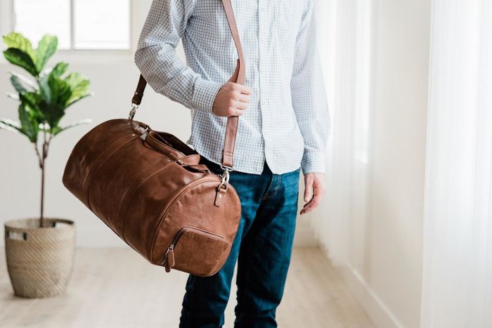 A brown leather oval-shaped bag with a long shoulder strap, slung over the shoulder of a model.