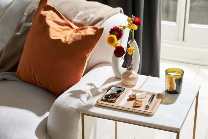 A photo of the catchall resting on an end table in the living room, with a phone charging and a variety of small items placed inside the tray.