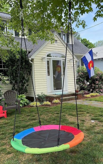 Circular swing hanging in a yard with a house and flag visible in the background