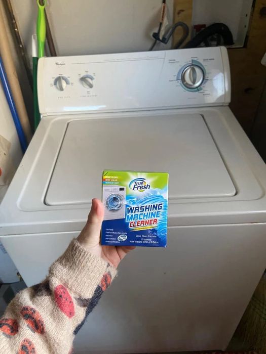 A person holding a box of washing machine cleaner in front of a washing machine