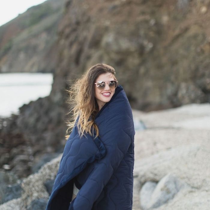 A model is wrapped in a blue quilted blanket, enjoying its warmth and comfort.