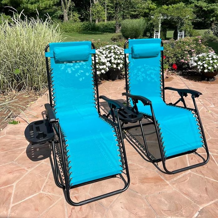 Two blue zero gravity chairs positioned on a patio, surrounded by lush greenery and blooming flowers