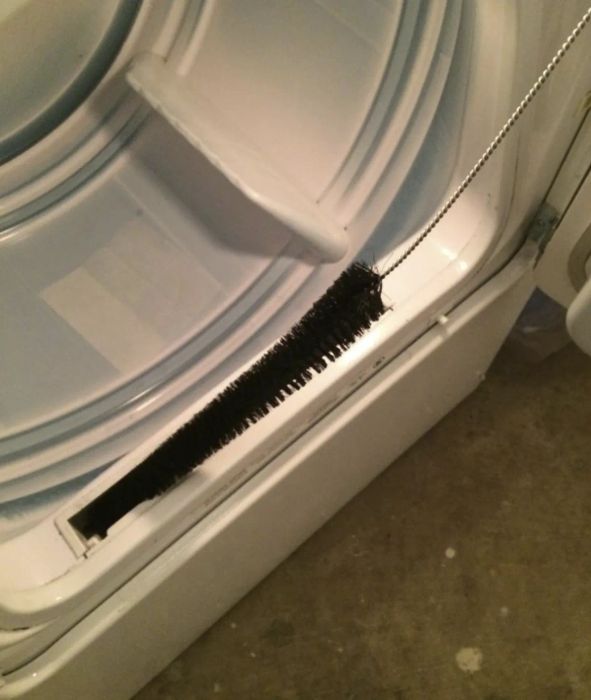 A reviewer holding a long, skinny dryer vent brush with bristles over the vent where the filter slides in