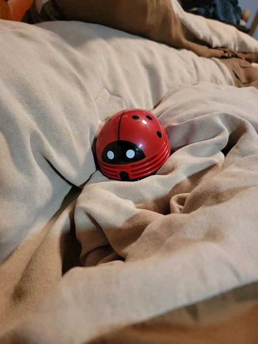 A ladybug-shaped vacuum placed on a cozy bed, perfect for efficient cleaning