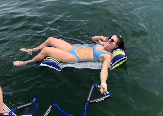 A reviewer is seen enjoying the float, which includes a neck pillow and leg support for added comfort