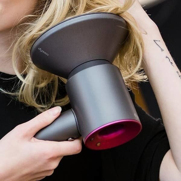 A model holds the hair dryer with a diffuser attachment, bringing it up to their hair.