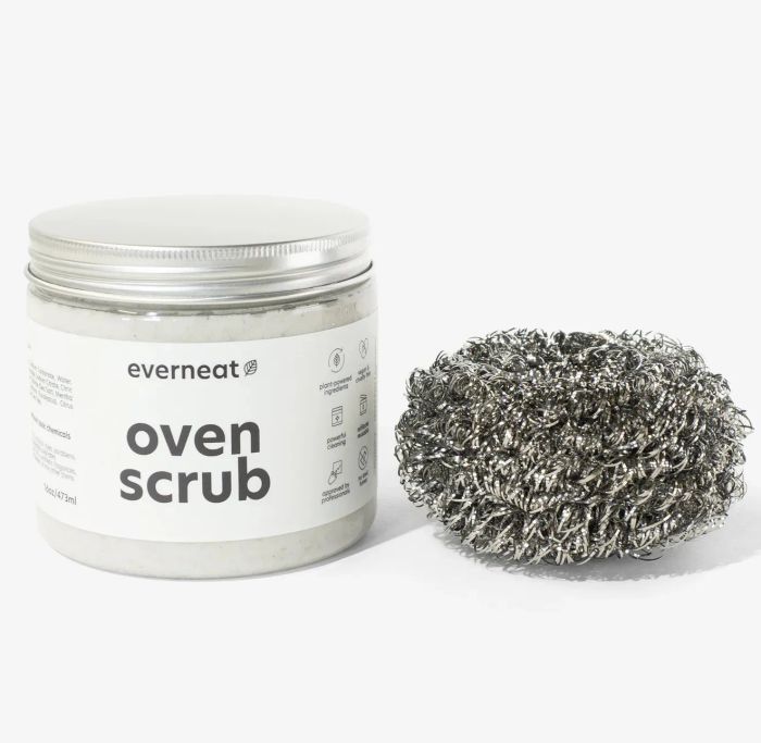 The jar of oven scrub placed beside a metallic scrubbing pad, ready for action