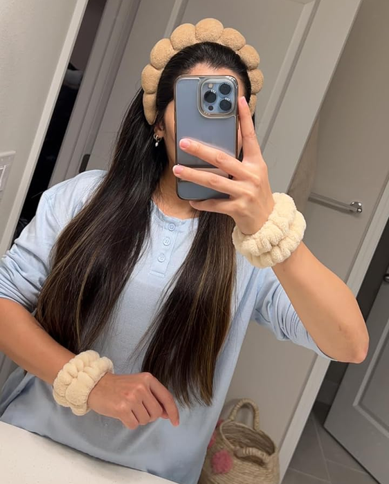A reviewer taking a mirror selfie in the bathroom, showcasing a puffy headband and matching wristbands with soft, round designs. She’s wearing a long-sleeve shirt.