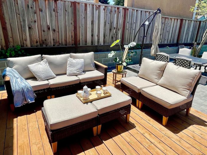 An outdoor seating area with a sofa, chairs, and a table bathed in sunlight, complemented by a potted plant and cushions on the furniture